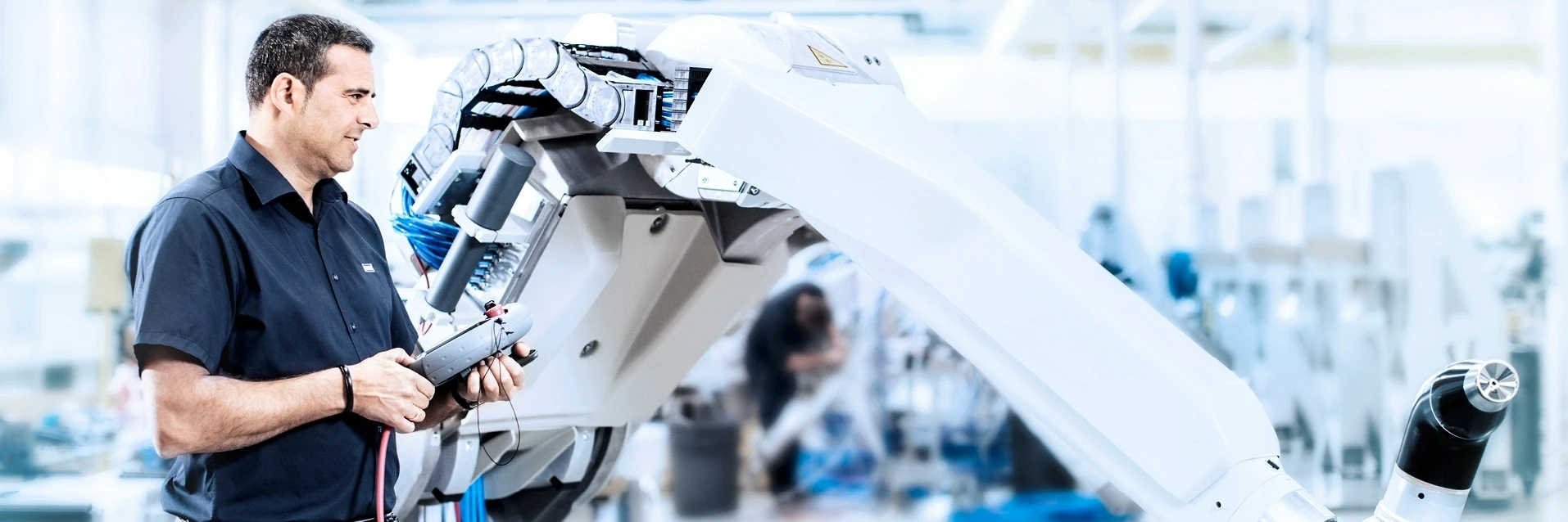 Engineer operating an industrial robot arm with a control device in a factory setting.