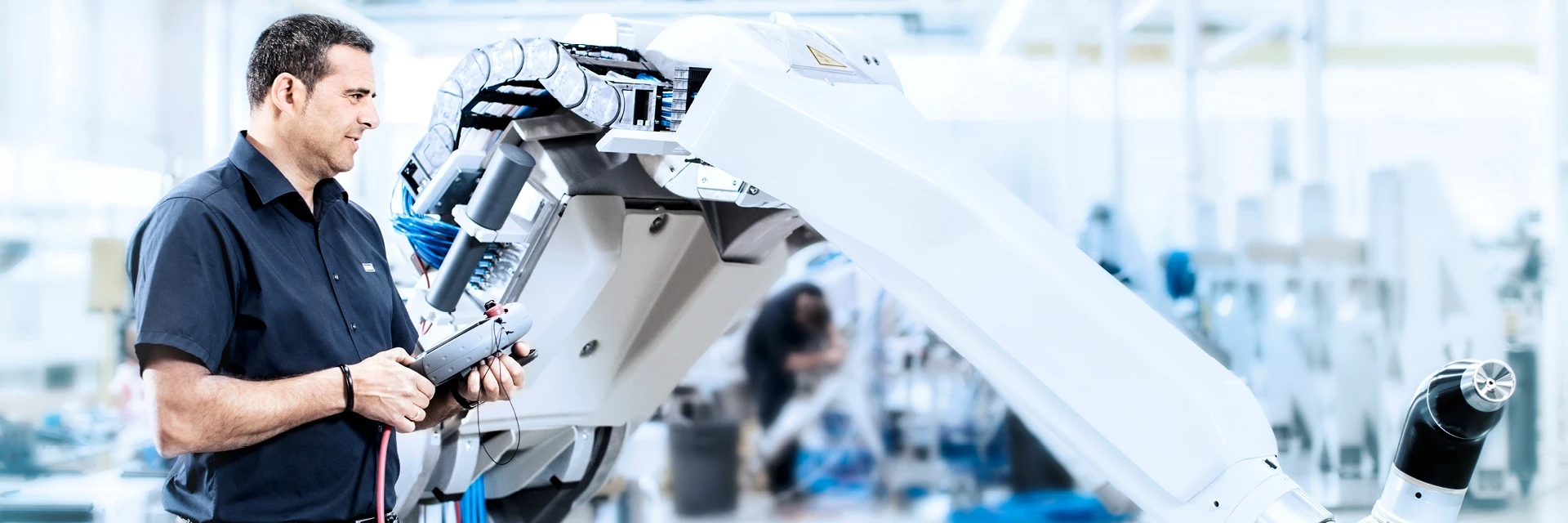 Engineer operating an industrial robot arm with a control device in a factory setting.