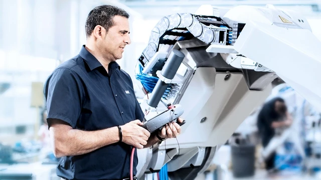 Ingenieur bedient einen Industrieroboterarm mit einem Steuergerät in einer Fabrikumgebung.